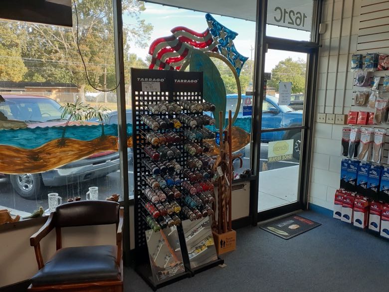 Shop interior detail: a tall rack of colorful Tarrago shoe polish, wooden walking sticks and a leather fitting chair by the painted window