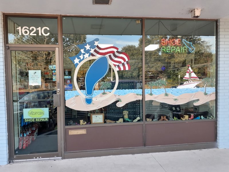 Close-up of the hand-painted shop window: a blue shoe logo, American flag and beach scene beside a neon SHOE REPAIR sign